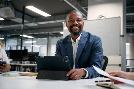 Téléchargez les photos : Trois hommes d'affaires multiraciaux heureux portant des vêtements d'affaires utilisant la technologie pendant la réunion au bureau - en image libre de droit