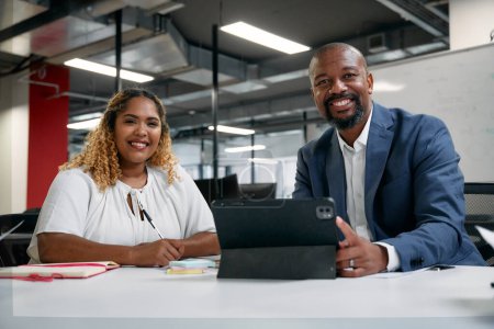 Foto de Dos personas de negocios multirraciales mirando a la cámara y sonriendo mientras usa la tableta digital en la oficina corporativa - Imagen libre de derechos