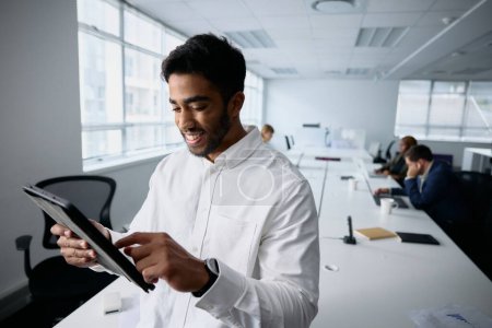 Foto de Feliz joven hombre de negocios usando ropa de negocios usando tableta digital por escritorio en la oficina - Imagen libre de derechos