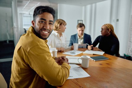 Foto de Cuatro felices jóvenes adultos multirraciales usando ropa de negocios hablando en la sala de reuniones en la oficina - Imagen libre de derechos
