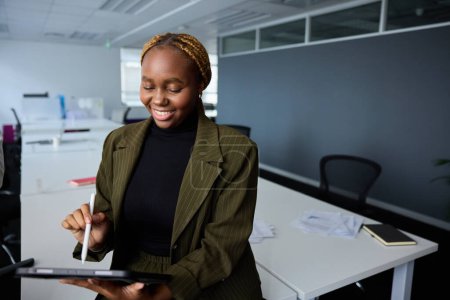 Foto de Joven empresaria con ropa de negocios sonriendo mientras usa tableta digital y pluma digitalizada en el escritorio en la oficina corporativa - Imagen libre de derechos