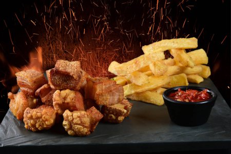 Photo for Fried pork skin crackling pancetta pururuca typical brazilian food with lemon and french fries with fire in the background - Royalty Free Image