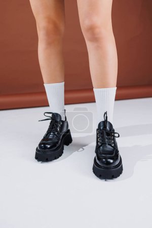 Schöne Frauenbeine in schwarzen Leder-Schnürloafern. Frauenbeine mit modischen Schuhen und weißen Socken. Lässige schwarze Damenschuhe