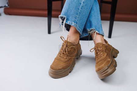 Foto de Close-up of female legs in blue jeans and suede brown sneakers. Women's leather casual sneakers - Imagen libre de derechos