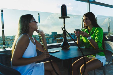 Photo for Girlfriends sit on the open terrace and smoke hookah, rest with girlfriends - Royalty Free Image
