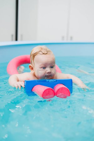Téléchargez les photos : Nager dans la piscine dès la naissance. Le garçon a appris à nager dans l'eau. Enfant heureux avec entraîneur en piscine jouant et s'amusant. Une famille saine et sportive avec un bébé - en image libre de droit