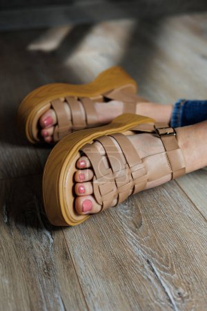Téléchargez les photos : Sandales en cuir beige sur les pieds des femmes. Pieds féminins dans des sandales décontractées confortables - en image libre de droit