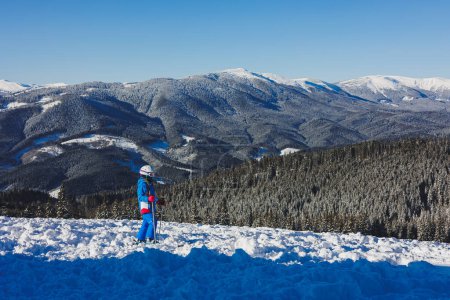 Une petite fille de 8 ans en costume de ski et sur des skis se dresse sur fond de montagnes enneigées. Station de ski