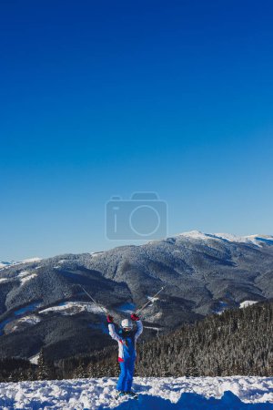 Una niña de 8 años con traje de esquí y esquís se levanta sobre el fondo de las montañas nevadas. Estación de esquí