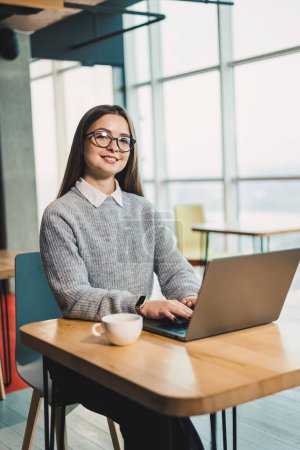 Linda mujer de negocios sentada en un escritorio en un espacio de trabajo moderno trabajando en un ordenador portátil. Proceso de trabajo de una mujer en la oficina