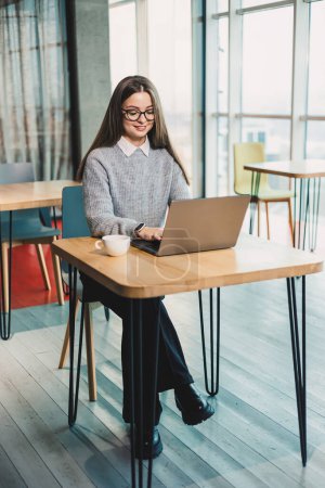 Nette Geschäftsfrau sitzt an einem Schreibtisch in einem modernen Arbeitsbereich und arbeitet an einem Laptop. Arbeitsprozess einer Frau im Büro