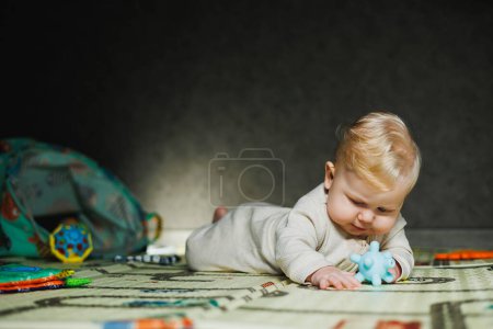 The child crawls on his stomach. A small 6-month-old baby is crawling on the rug and smiling. A boy plays with a toy on the floor.