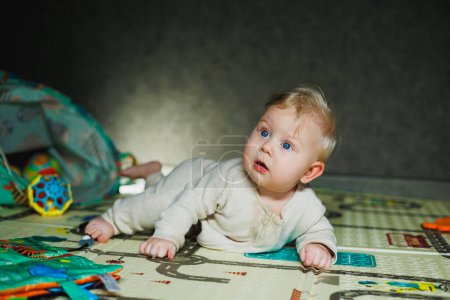 Das Kind krabbelt auf seinem Bauch. Ein kleines, 6 Monate altes Baby krabbelt auf dem Teppich und lächelt. Ein Junge spielt mit einem Spielzeug auf dem Fußboden.