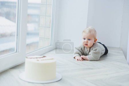 A smiling 6-month-old boy is crawling towards a delicious cake.