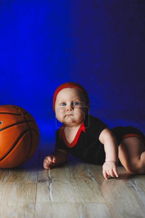 Bebé 7 meses con una pelota de baloncesto. Deportes para niños. Ropa de algodón para bebés
