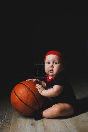 Bebé 7 meses con una pelota de baloncesto. Deportes para niños. Ropa de algodón para bebés