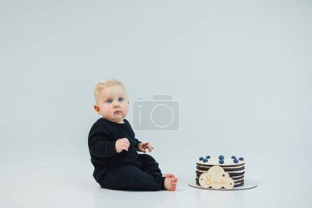 a little boy of 8 months on a white background lies near a cake. sweet cake for a little boy.