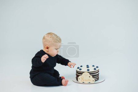Ein kleiner Junge von 8 Monaten auf weißem Hintergrund liegt neben einer Torte. süße Torte für einen kleinen Jungen.