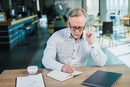 Photo for Mature businessman working while sitting in the office. A middle-aged executive is working in the office using a laptop. Emotional businessman - Royalty Free Image