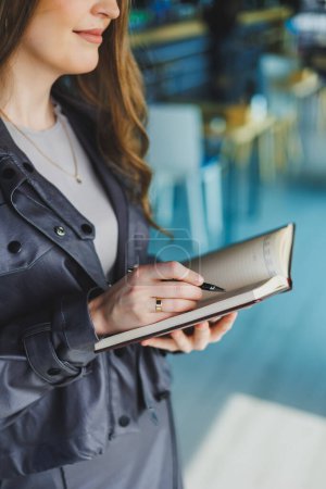 Una joven en la oficina toma notas en un cuaderno. Una mujer de negocios trabaja en un espacio de trabajo moderno