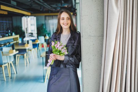 Young modern woman in the office with flowers in her hands. Tulips in the hands of a woman