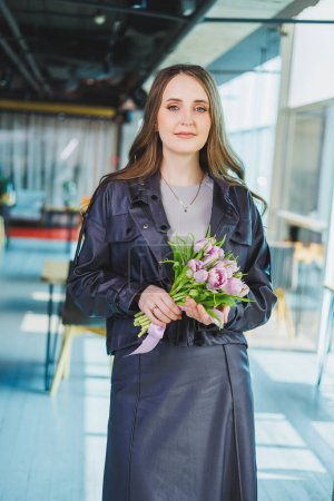 Young modern woman in the office with flowers in her hands. Tulips in the hands of a woman