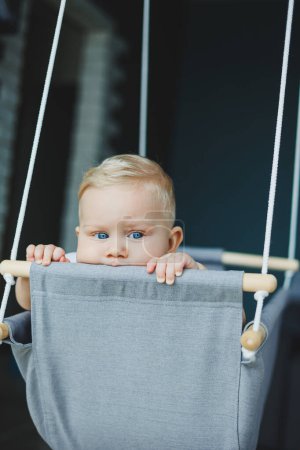 Baby boy swings on a swing at home. A child rides on a swing at home