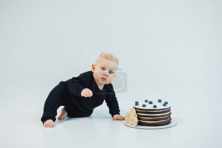 un petit garçon de 8 mois sur fond blanc se trouve près d'un gâteau. gâteau sucré pour un petit garçon.