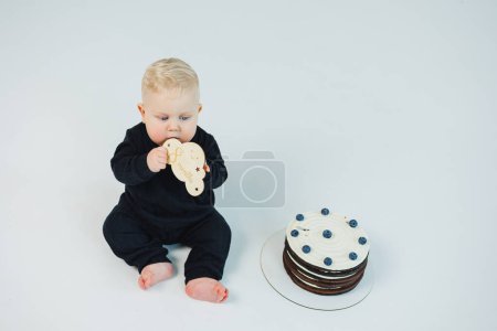 Ein kleiner Junge von 8 Monaten auf weißem Hintergrund liegt neben einer Torte. süße Torte für einen kleinen Jungen.