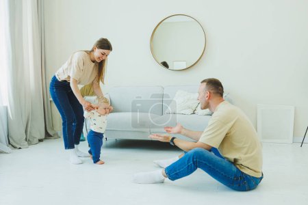 A young married couple is having fun playing with a small child in a modern living room together. Smiling parents mom and dad enjoying spending time with cute funny baby boy at home.