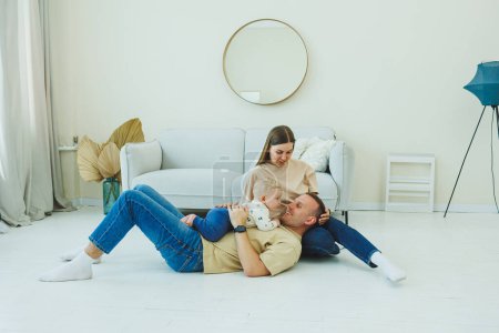 A young married couple is having fun playing with a small child in a modern living room together. Smiling parents mom and dad enjoying spending time with cute funny baby boy at home.