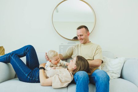 Ein junges Ehepaar hat Spaß beim gemeinsamen Spielen mit einem kleinen Kind in einem modernen Wohnzimmer. Lächelnde Eltern Mama und Papa genießen die Zeit mit süßen lustigen Baby-Jungen zu Hause.