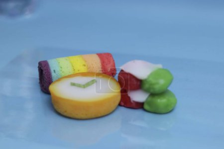 Foto de Mini pastel de rollo de arco iris con un sabor súper delicioso, Lapindo kue lumpur es un pastel húmedo indonesio tradicional, y deliciosa merienda del mercado, fondo azul. - Imagen libre de derechos