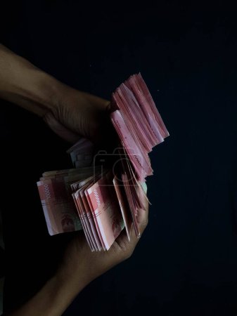 Téléchargez les photos : Mains avec des millions de rupiahs sur un fond noir - en image libre de droit
