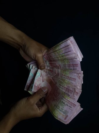 Téléchargez les photos : Mains avec des millions de rupiahs sur un fond noir - en image libre de droit