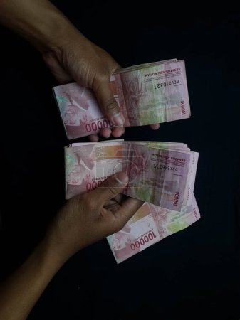 Foto de Una mano masculina sostiene millones de rupias indonesias sobre un fondo negro - Imagen libre de derechos