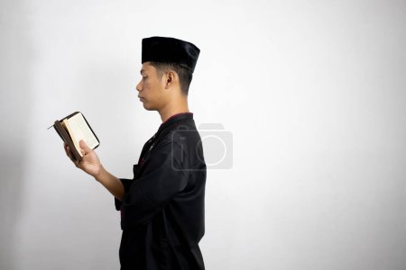 Téléchargez les photos : Jeune homme musulman asiatique portant des vêtements traditionnels et tenant un coran - en image libre de droit