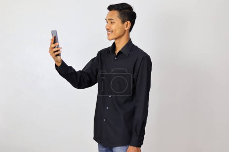Téléchargez les photos : Asiatique jeune homme en bleu marine chemise en utilisant smartphone sur fond blanc - en image libre de droit