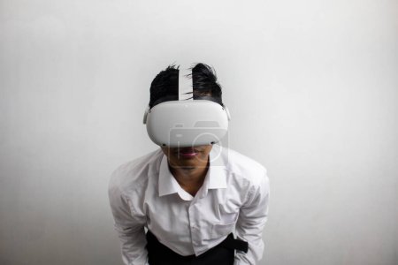 Téléchargez les photos : Jeune homme en chemise blanche soignée utilisant casque de réalité virtuelle. Isolé sur fond blanc portrait studio. VR, futur, gadgets, technologie, éducation en ligne, apprentissage, concept de jeu vidéo - en image libre de droit