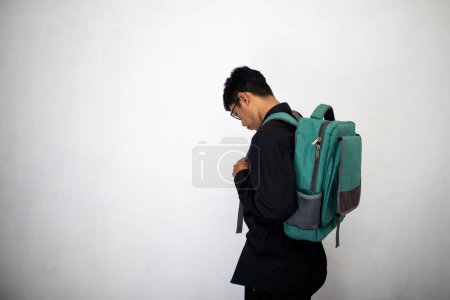 Foto de Hombre asiático con ropa negra limpia está llevando una mochila verde sobre un fondo blanco. un estudiante llevando una bolsa con confianza. - Imagen libre de derechos