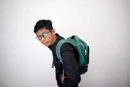 Foto de Hombre asiático con ropa negra limpia está llevando una mochila verde sobre un fondo blanco. un estudiante llevando una bolsa con confianza. - Imagen libre de derechos