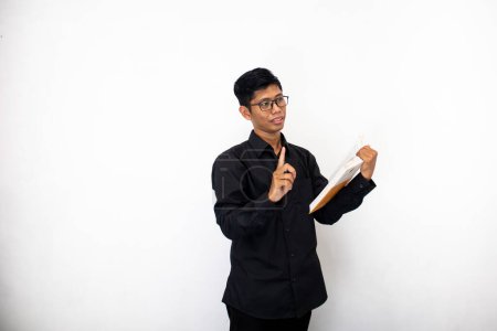 Foto de Asiático hombre en limpio negro ropa en gafas con libro en mano es estudiar - Imagen libre de derechos