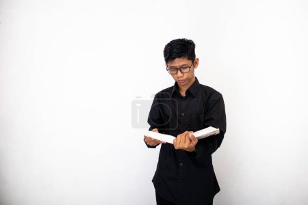 Photo for Asian man in neat black clothes in glasses with book in hands is studying - Royalty Free Image