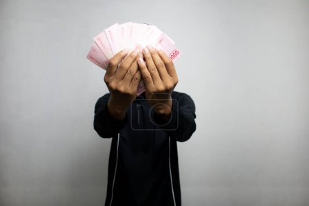 Téléchargez les photos : Beau asiatique homme en noir vêtements tenant pile d'argent, fond de studio blanc - en image libre de droit
