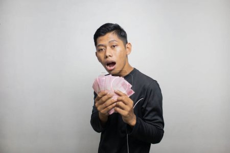 Téléchargez les photos : Beau asiatique homme en noir vêtements tenant pile d'argent, fond de studio blanc - en image libre de droit
