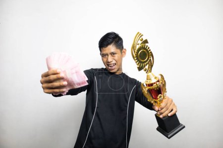 Téléchargez les photos : Beau asiatique homme en vêtements noirs tenant coupe trophée d'or avec pile d'argent, fond de studio blanc - en image libre de droit