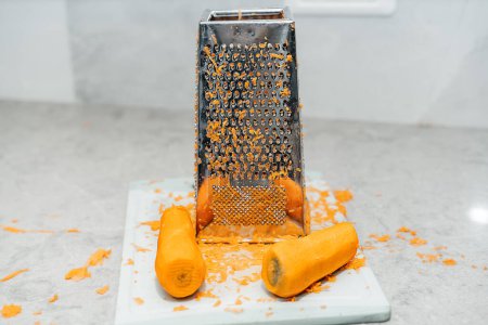 Foto de Image of a grated carrot and a grater with peelings sprinkled around. Lived-in Interior with mess, real authentic life, reality, true life. Healthy organic food. - Imagen libre de derechos