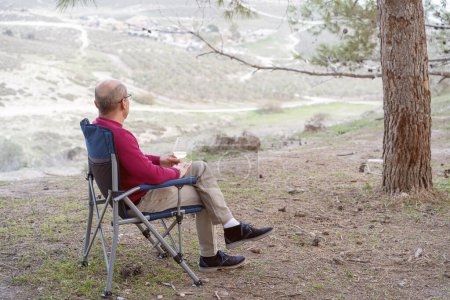 Photo for Man sitting on folding chair with glass of wine, admiring the beautiful views of nature. - Royalty Free Image