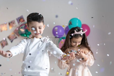 Paper multicolored confetti falling on heads of smiling happy children on birthday party.