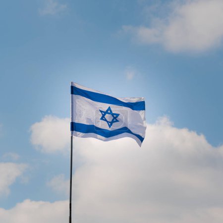 Téléchargez les photos : Drapeau israélien agitant dans le vent contre le ciel bleu et les nuages blancs par une journée ensoleillée. Jour de l'indépendance Israël - Yom Haatzmaut . - en image libre de droit